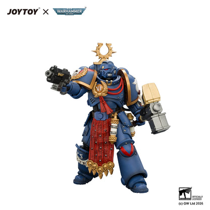 A detailed collectible action figure of a blue Space Marine warrior with gold and red accents, posed holding a black weapon in one hand and a hammer in the other, on a plain white background with JOYTOY and Warhammer 40k branding at the top.